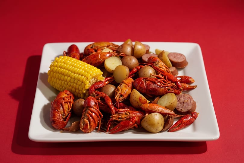 Boiled crawfish, corn on the cob, potatoes, and sausage on a white rectangular plate.