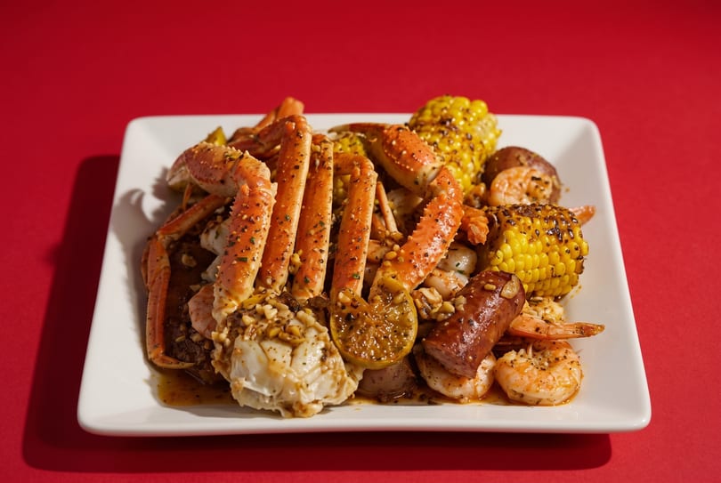 A seafood boil with crab legs, shrimp, corn, sausage, and potatoes on a white plate.